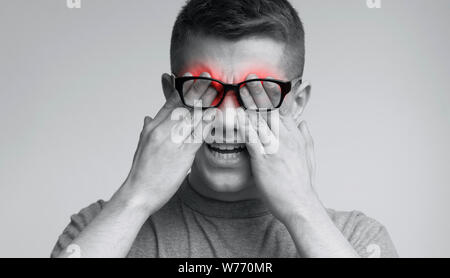 Young caucasian man in glasses rubbing his eyes Stock Photo