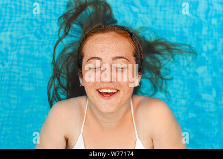 Teenager. Young woman with freckles into the swimming pool. Smiling.