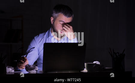 Tired man is working on laptop in darkness Stock Photo