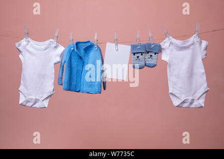 New born baby grows, jumpers, socks hanging on a clothes line against pink Stock Photo