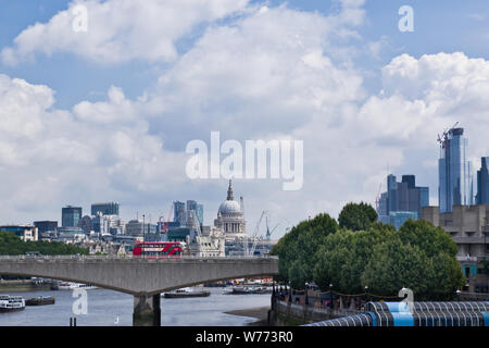 A red London bus crosses Waterloo bridge over the river Thames, with St Pauls cathedral visible on the skyline. London, UK. Stock Photo