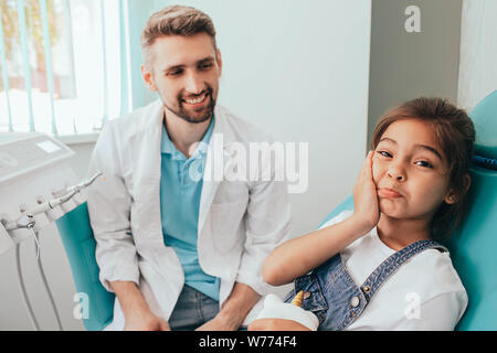 mixed race little girl showing toothache at camera. Sadness child in dental chair
