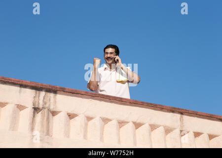 South Indian man talking on a mobile phone and punching the air Stock Photo