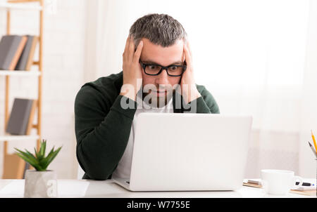 Shocked caucasian man is sitting in front of laptop Stock Photo