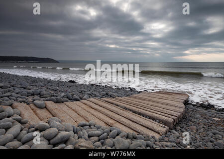 A huge rolling wave his the beach at westward ho! in Devon on a cloudy day. There is a stone path leading to the sea. Stock Photo