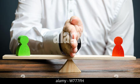 A man divides with his palm two figures of people of opponents on the scales. To reason and settle the conflict between the parties, the solution of t Stock Photo
