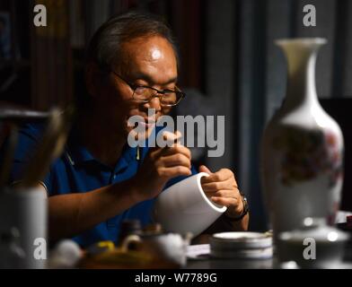 (190805) -- NANCHANG, Aug. 5, 2019 (Xinhua) -- Mao Guanghui works on a piece of porcelain at his studio in Jingdezhen, east China's Jiangxi Province, Aug. 1, 2019. Mao Guanghui, a 56-year-old senior master of arts and crafts in Jiangxi Province, has been devoting himself to porcelain painting since the age of 13. As a third-generation disciple of Deng Bishan (1874-1930), one of the 'Eight Friends of Zhushan', a group of Jingdezhen artisans widely noted for their innovations in porcelain painting, Mao inherited not only the skills but also the art of creating porcelain painting pieces.     The Stock Photo