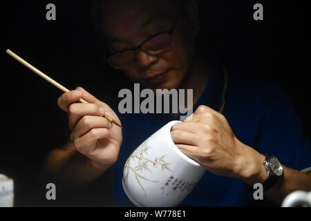(190805) -- NANCHANG, Aug. 5, 2019 (Xinhua) -- Mao Guanghui works on a piece of porcelain at his studio in Jingdezhen, east China's Jiangxi Province, Aug. 1, 2019. Mao Guanghui, a 56-year-old senior master of arts and crafts in Jiangxi Province, has been devoting himself to porcelain painting since the age of 13. As a third-generation disciple of Deng Bishan (1874-1930), one of the 'Eight Friends of Zhushan', a group of Jingdezhen artisans widely noted for their innovations in porcelain painting, Mao inherited not only the skills but also the art of creating porcelain painting pieces. The Stock Photo