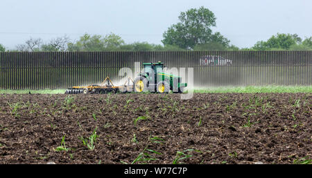 A Customs and Border Protection Agent vehicle patrols the border wall near Brownsville, Texas, whilst a farmer ploughs his field. Stock Photo