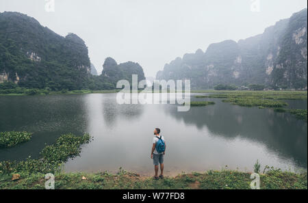 Caucasian man overlooking limestone mountains in Ninh Binh province, Vietnam. Cloudy day, reflection in water Stock Photo