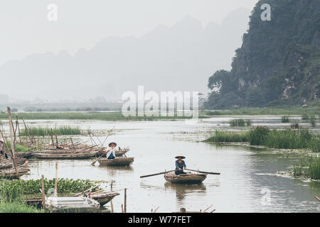 Ninh Binh, Vietnam - May 2019: Vietnamese woman in a wooden rowing boat going through Trang An nature park. Stock Photo