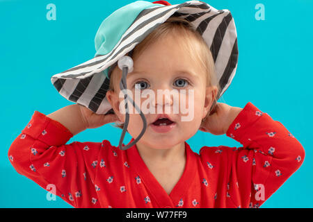Little girl putting on hat over blue Stock Photo