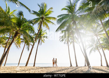 Couple standing on sandy beach among palm trees on sunny morning at seaside