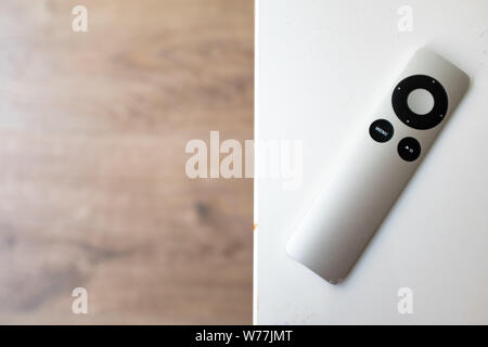 Grey remote control on a white table over a wooden blurry background Stock Photo