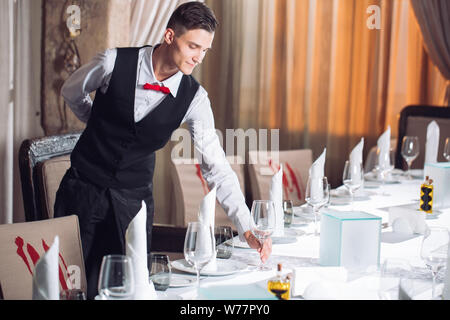 Waiter serving table in the restaurant preparing to receive guests. Stock Photo