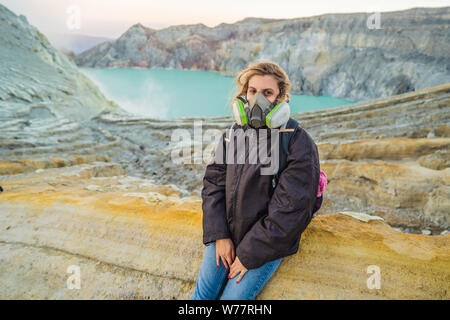 Young woman tourist sitting at the edge of the crater of the Ijen volcano or Kawah Ijen on the Indonesian language. Famous volcano containing the Stock Photo