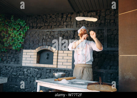 Skilled chef preparing dough for pizza rolling with hands and throwing up. Stock Photo