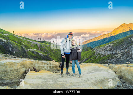 Young tourist man and woman stand at the edge of the crater of the Ijen volcano or Kawah Ijen on the Indonesian language. Famous volcano containing Stock Photo