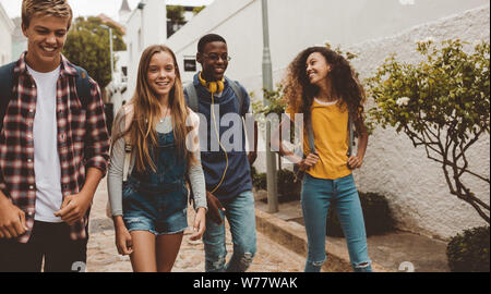 Multiethnic college friends walking in street. Happy boys and girls walking in street wearing college bags. Stock Photo