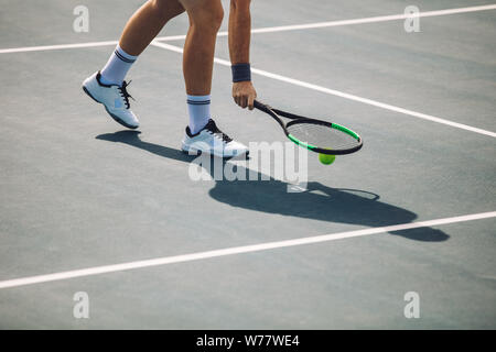 Cropped shot of sportsperson on tennis court picking the ball with racket. Male tennis player pick up the ball on hard court. Stock Photo