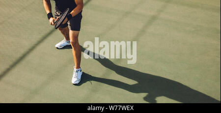 Tennis player playing tennis on hard court. Young man in sports wear standing on hard tennis court ready to return the serve during a game. Stock Photo