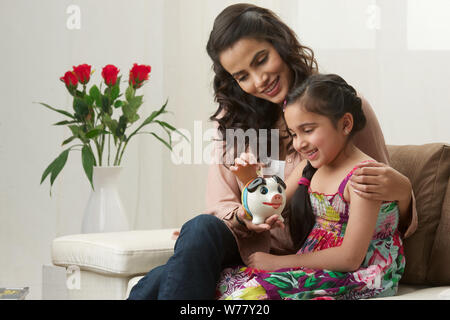 Girl putting coin into a piggy bank with her mother Stock Photo