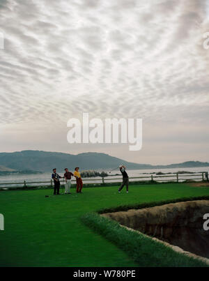 Man taking a swing with a golf club while playing golf with his friends on a golf course. Stock Photo