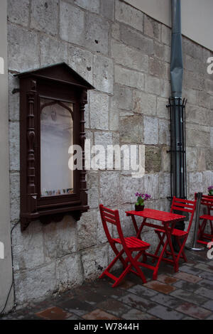 Cozy outdoor cafe red chairs and table after summer rain near brick building wall with menu screen in dark brown wooden frame. Stock Photo