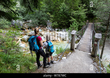 Mother and son crossing a wooden suspension bridge over beautiful turquoise Soca river while trekking on Soca trail, Bovec, Slovenia, Europe