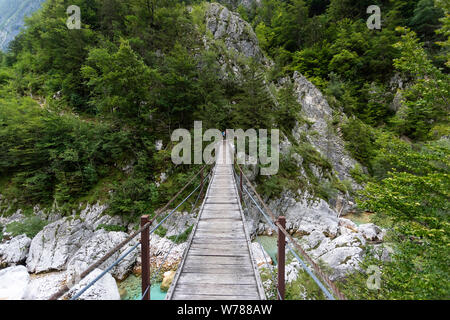 Mother and son crossing a high wooden suspension bridge over beautiful turquoise Soca river while trekking on Soca trail, Bovec, Slovenia, Europe