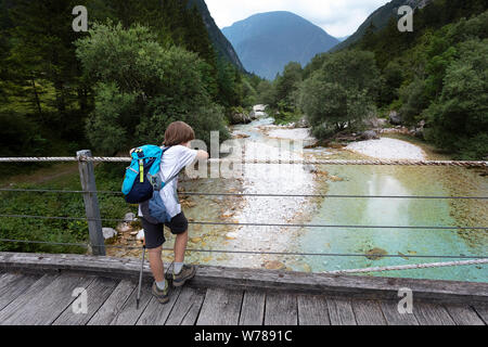 Cute young boy crossing a wooden suspension bridge over beautiful turquoise Soca river while trekking on Soca trail, Bovec, Slovenia, Europe