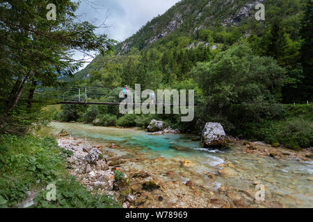 Mother and son crossing a wooden suspension bridge over beautiful turquoise Soca river while trekking on Soca trail, Bovec, Slovenia, Europe