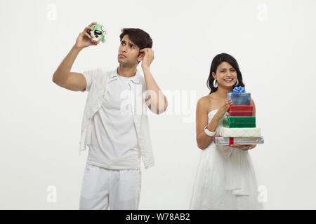 Young man looking piggy bank with her wife holding gift boxes Stock Photo