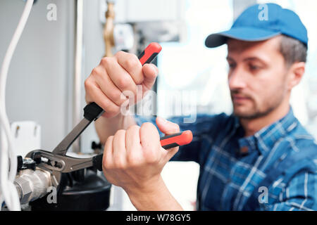 Hands of young contemporary technician with pliers fixing nut on pipe Stock Photo