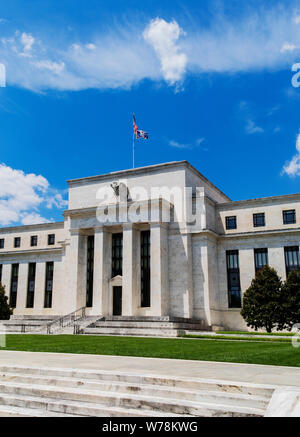 Exterior view of Federal Reserve Board of Governors Building facade entrance with eagle stone statue and American flags over a blue cloudscape sky. Stock Photo