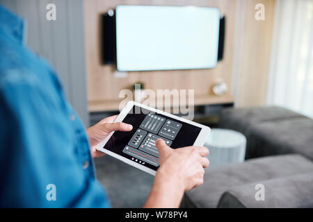 Hands of young man holding tablet with smart remote control system Stock Photo