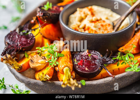 Baked carrots, beets, zucchini and yam with hummus in a dark dish. Stock Photo