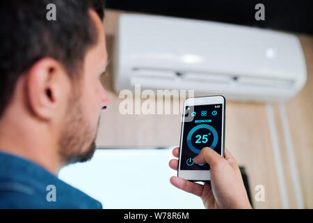 Young man using smart application to adjust temperature of air conditioner Stock Photo