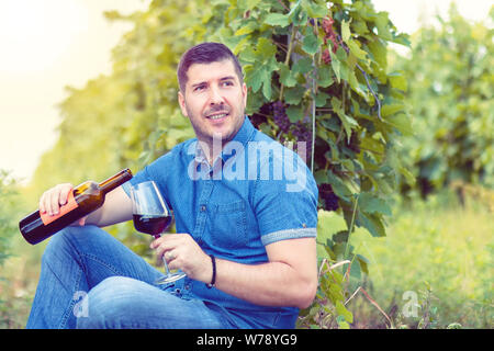 Smiling man having fun holding a glass of red wine in hand at sunset in vineyard – happy caucasian male enjoying harvest time drinking wine at winery Stock Photo