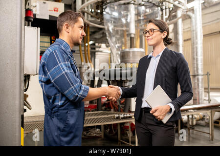 Young female partner shaking hand of engineer of chemical processing factory Stock Photo