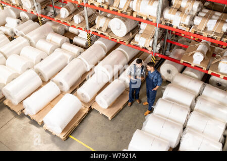 Two young engineers of large processing factory working in warehouse Stock Photo