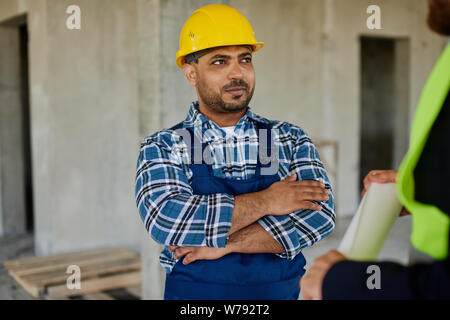 Two engineers discuss work related questions together holding folded blueprint. Stock Photo