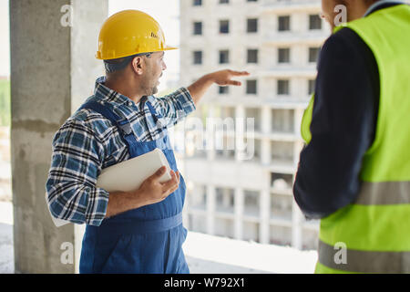 Two engineers discuss work related questions together holding folded blueprint. Stock Photo