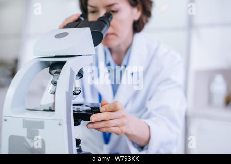 Female scientist works in the lab with the microscope shot in the close up. Stock Photo