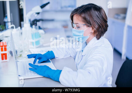 Scientist typing into the computer wearing all the safety wear. Stock Photo