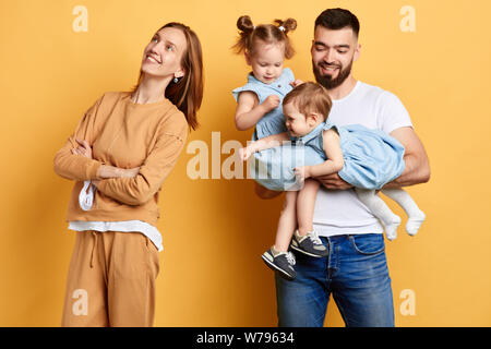 happy young mother standing back to her husband and her little daughters. close up photo. isolated yellow background. kids doesn't want to play with d Stock Photo