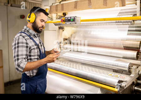 Young serious quality control engineer using tablet to check parameters Stock Photo