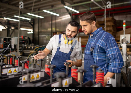 Bearded engineer explaining principles of work of new processing equipment Stock Photo