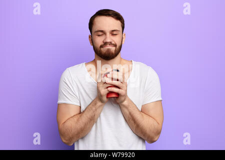 happy handsome man with closed eyes holding hot morning coffee. guy enjoying drinking takeaway coffee. time for coffee break, free time, spare time, l Stock Photo