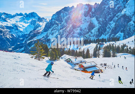 The skiers, making downhill from the Zwieselalm mountain, surrounded by rocky Dachstein West Alps, Gosau, Austria Stock Photo